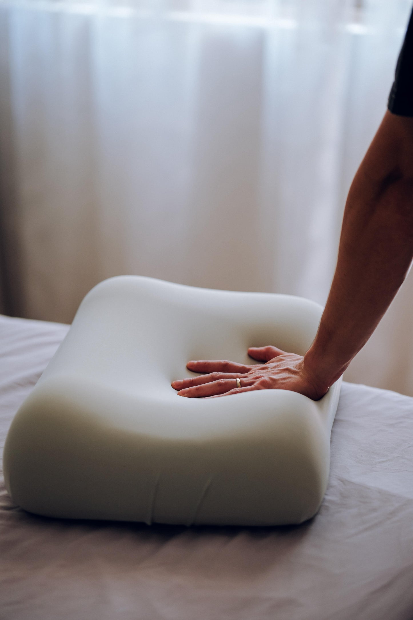 Person touching a white pillow on a bed with a blurred background
