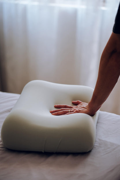 Person touching a white pillow on a bed with a blurred background